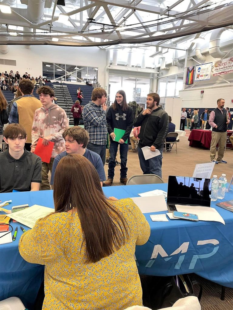 A line of students waiting to talk to a representative talking amongst each other.