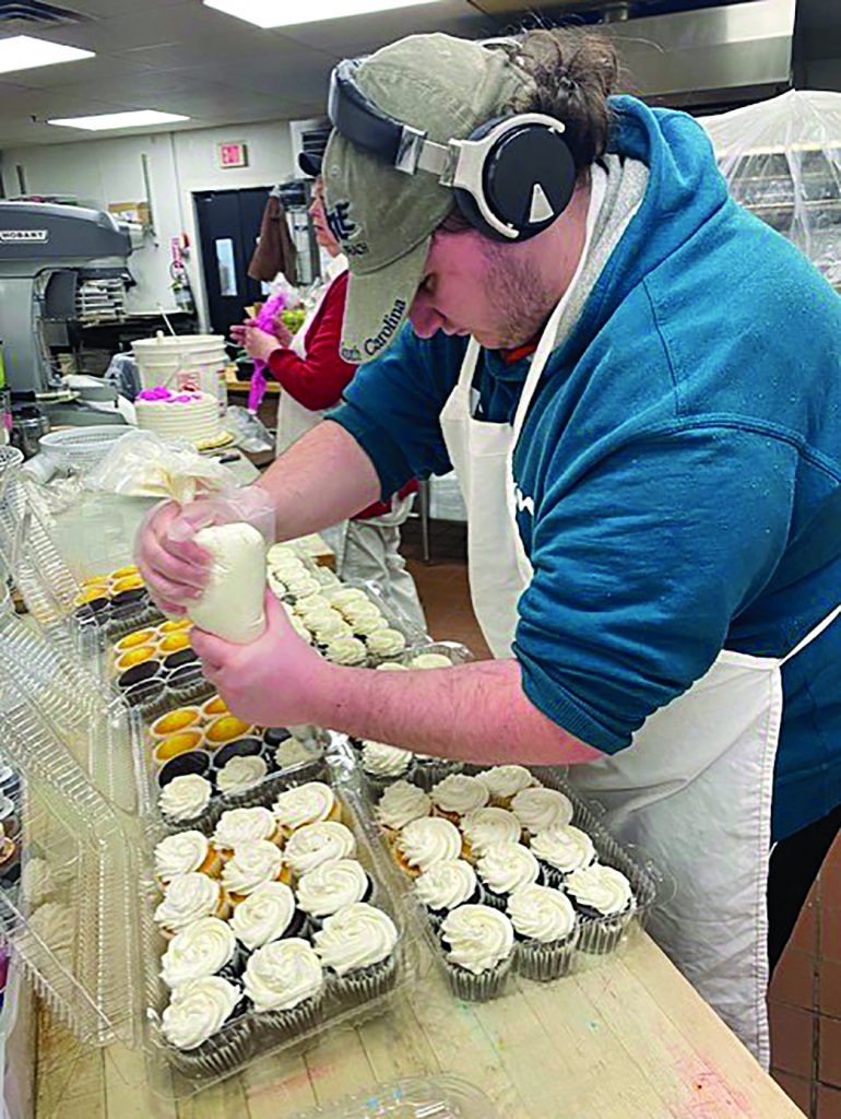 A teen student frosts cupcakes in a kitchen setting.