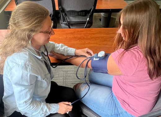 An adult student performs a blood pressure check on another student.