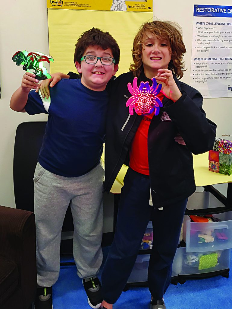 Two students contort their faces while holding spider and dinosaur toys.