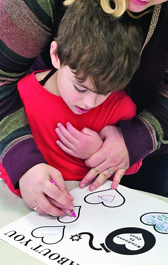 A young student receives help from a teacher in coloring a valentine.