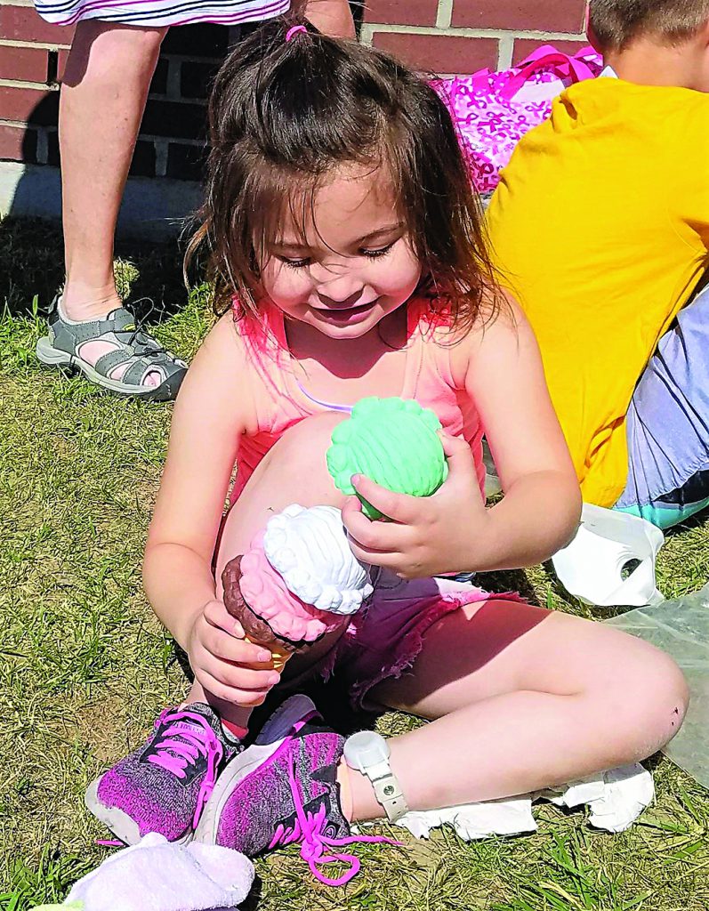 A young student plays outdoors with a large plastic ice cream cone toy.