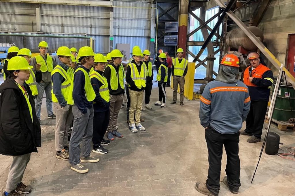 Students dressed in equipment equipment listen to two Alcoa employees during their tour.