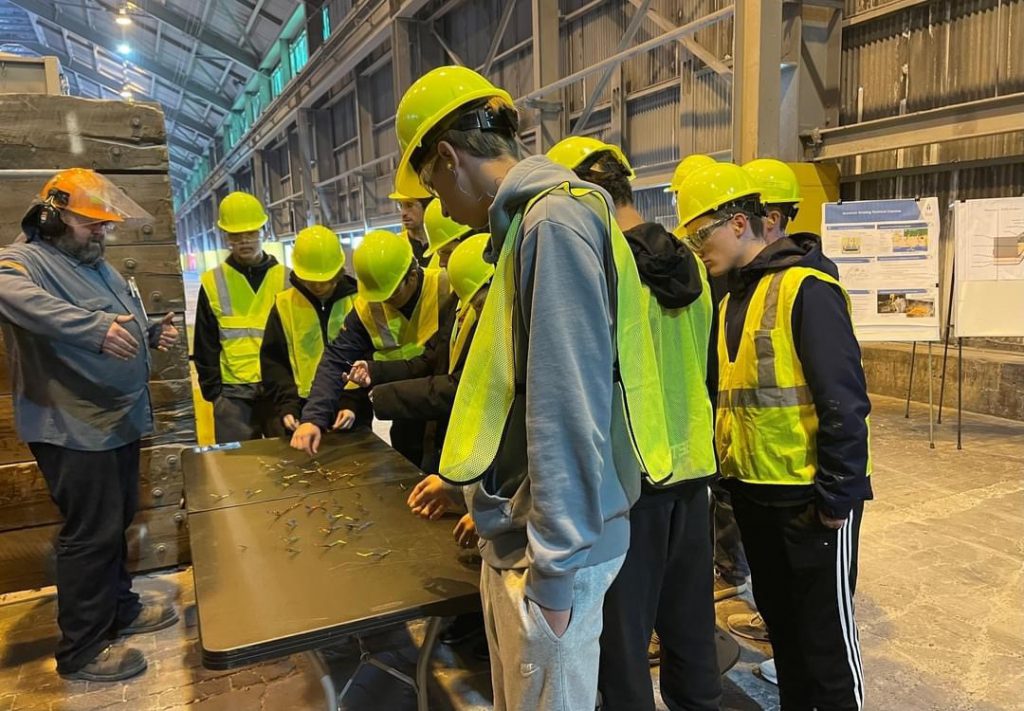 Students wearing safety equipment peer over a table to examine pieces of aluminum at the Alcoa plant.