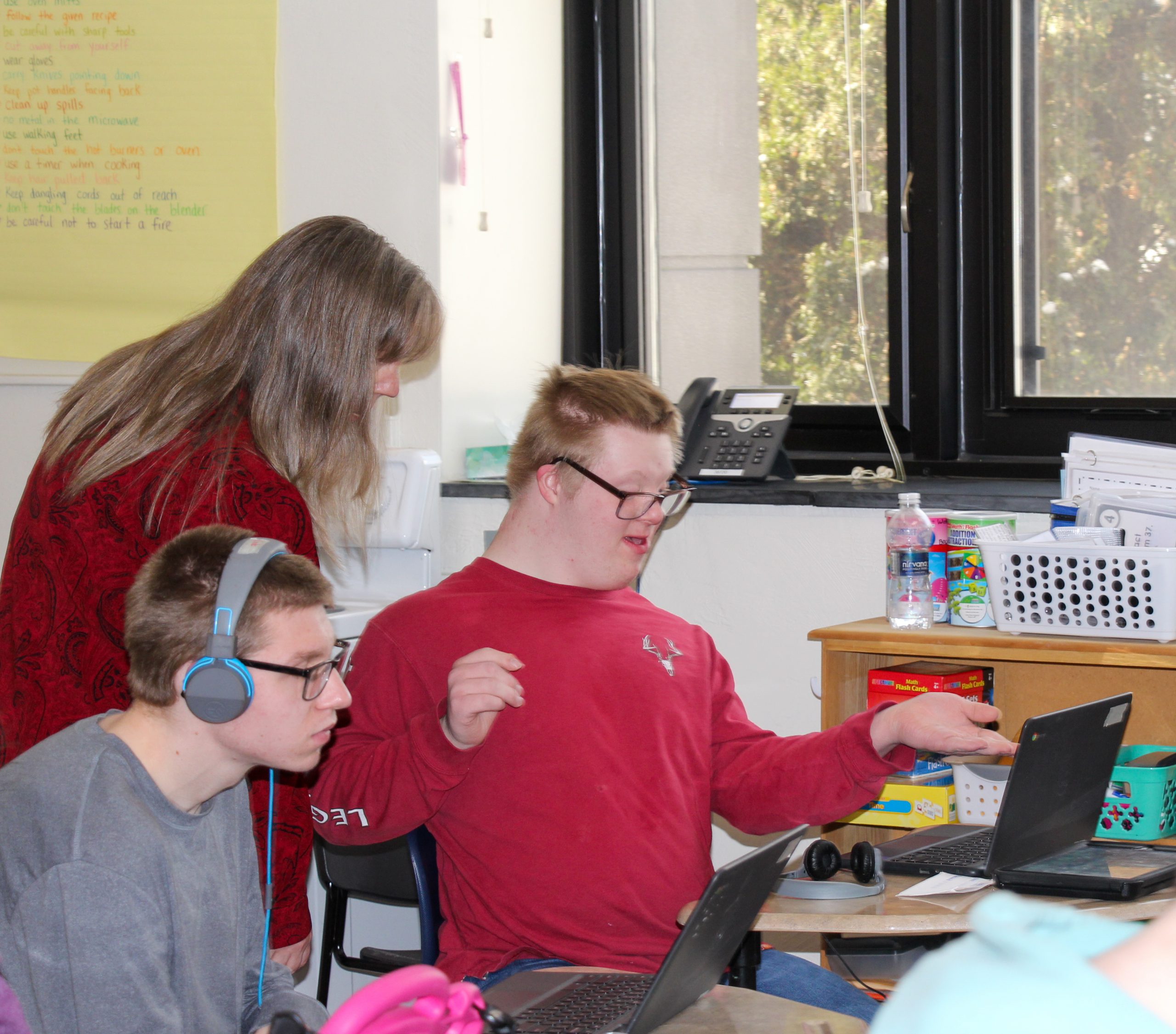 student in classroom with teacher looking on