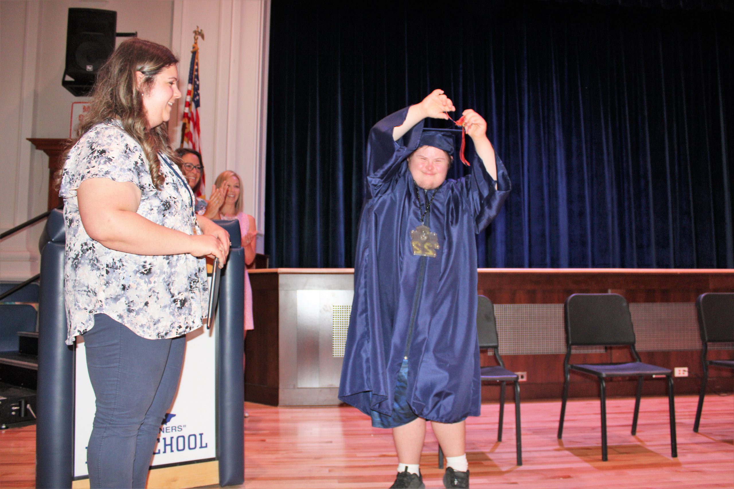 student in graduation cap and gown cheering from stage