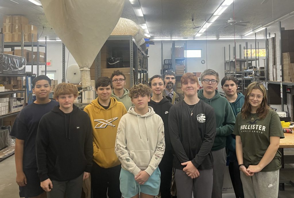 Several students stand together in a supply warehouse at the Queenaire plant.